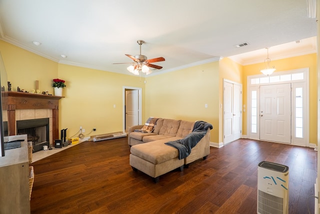 living area featuring a ceiling fan, baseboards, ornamental molding, a tile fireplace, and dark wood-style floors