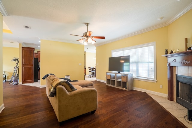 living room with ornamental molding, wood finished floors, a ceiling fan, and a tile fireplace