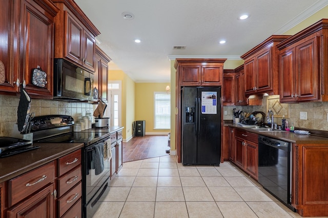 kitchen with a sink, dark countertops, crown molding, visible vents, and black appliances