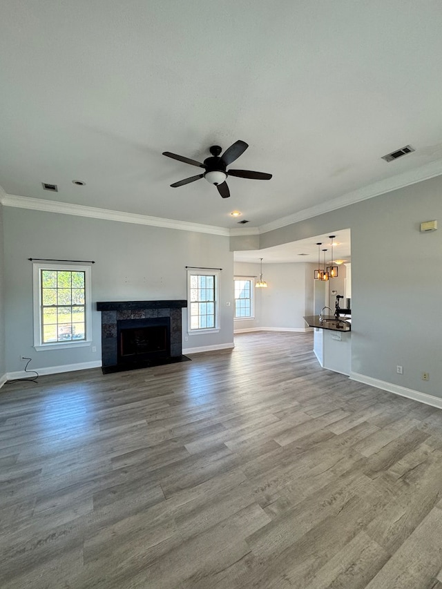 unfurnished living room with ceiling fan with notable chandelier, a fireplace, crown molding, and a wealth of natural light