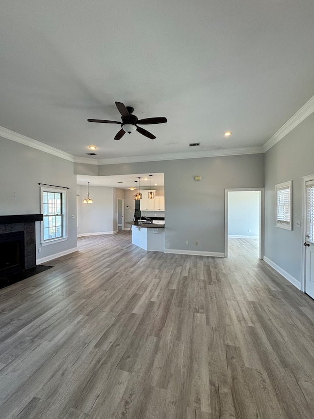 unfurnished living room featuring ornamental molding, light hardwood / wood-style floors, a tiled fireplace, and ceiling fan with notable chandelier