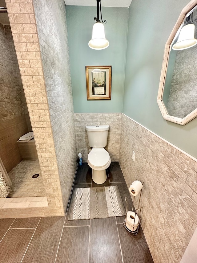 bathroom featuring toilet, tile walls, and a tile shower