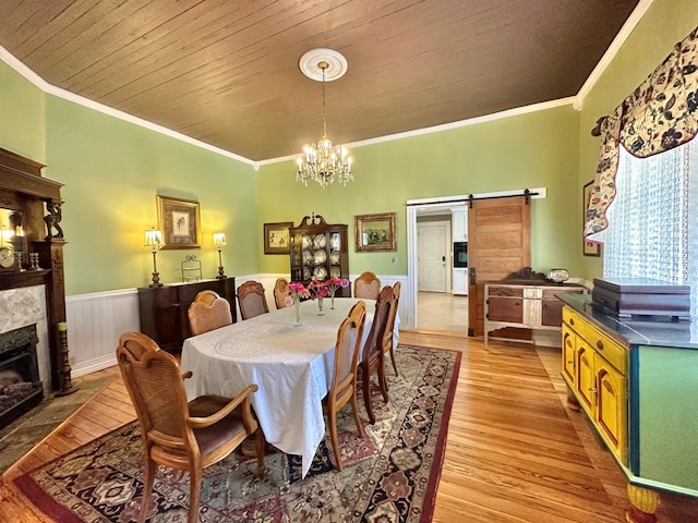 dining space with an inviting chandelier, light hardwood / wood-style floors, a barn door, a fireplace, and ornamental molding