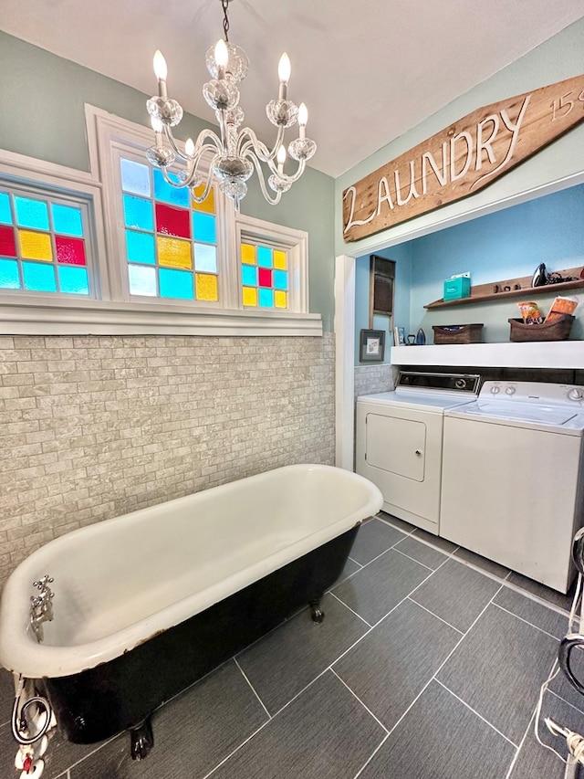 bathroom with washer and dryer, tile patterned flooring, a tub to relax in, and a notable chandelier