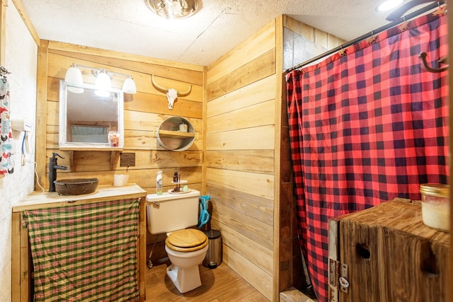 bathroom featuring wood walls, wood-type flooring, a textured ceiling, and toilet