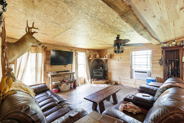 living room with a wood stove, ceiling fan, wood walls, cooling unit, and hardwood / wood-style flooring