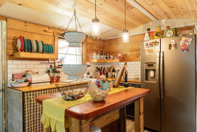 kitchen featuring lofted ceiling, stainless steel refrigerator with ice dispenser, wooden walls, decorative backsplash, and decorative light fixtures