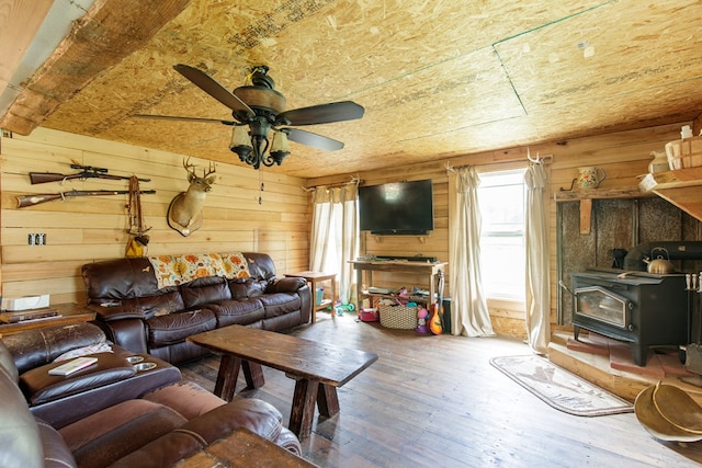 living room with a wood stove, wooden walls, ceiling fan, and wood-type flooring