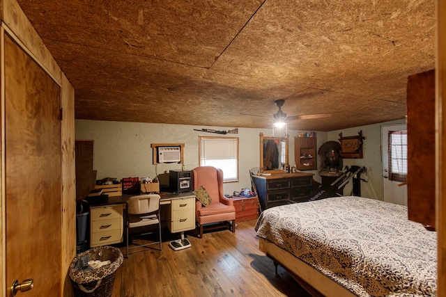 bedroom with a wall mounted AC, hardwood / wood-style flooring, and ceiling fan