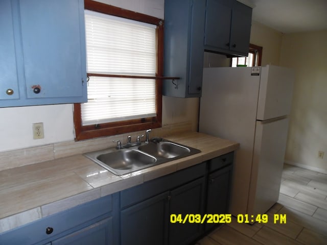 6 Prince Cv, Valdosta, GA 31601 - kitchen with a sink, tile countertops, blue cabinetry, baseboards, and freestanding refrigerator