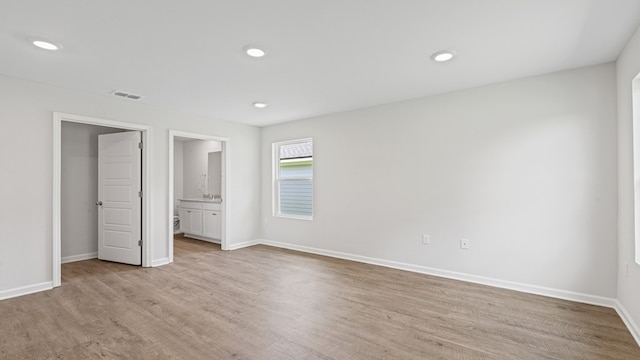 unfurnished bedroom with ensuite bathroom and light hardwood / wood-style floors