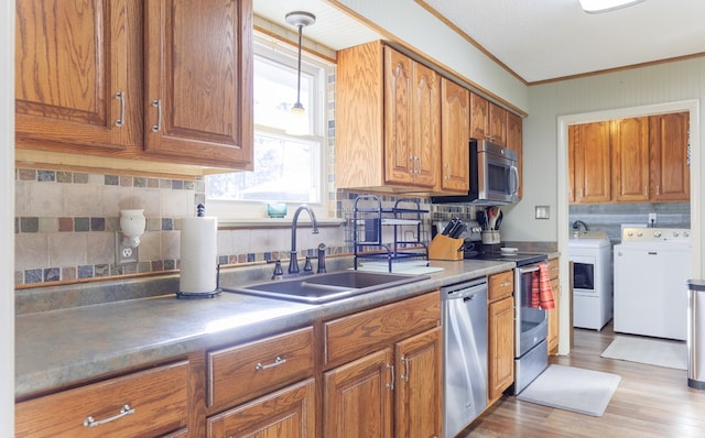 kitchen with stainless steel appliances, separate washer and dryer, hanging light fixtures, light hardwood / wood-style flooring, and sink