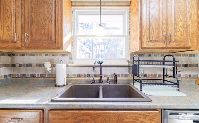 kitchen featuring stainless steel dishwasher, sink, hanging light fixtures, and tasteful backsplash