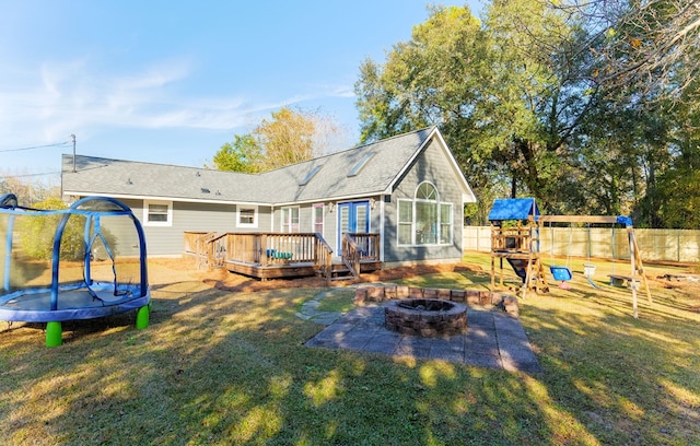 rear view of property featuring a fire pit, a trampoline, a yard, a playground, and a wooden deck