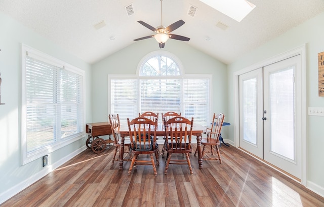 dining room with ceiling fan, vaulted ceiling with skylight, hardwood / wood-style flooring, a healthy amount of sunlight, and french doors