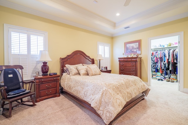 bedroom with a closet, light carpet, ceiling fan, a tray ceiling, and a walk in closet