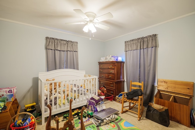 bedroom featuring ceiling fan, crown molding, a crib, and carpet floors