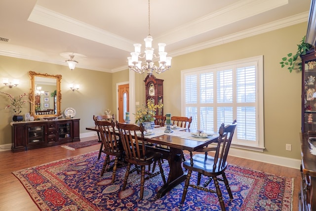 dining area with hardwood / wood-style flooring, a chandelier, a tray ceiling, and ornamental molding