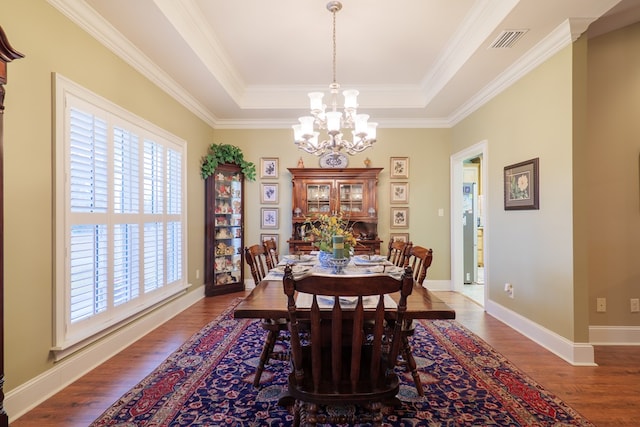 dining area with dark hardwood / wood-style flooring, a raised ceiling, ornamental molding, and a notable chandelier