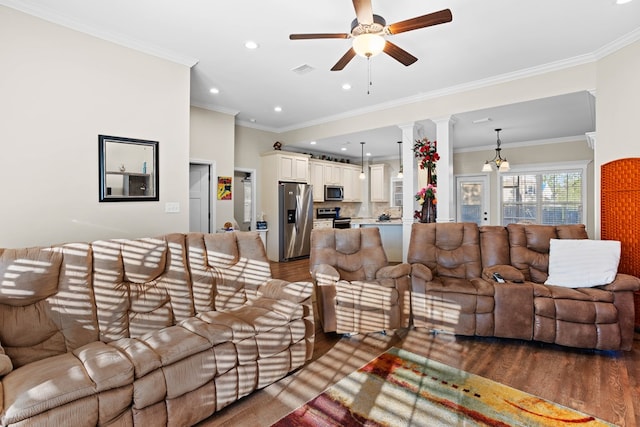 living room featuring ceiling fan with notable chandelier, dark hardwood / wood-style flooring, ornate columns, and crown molding