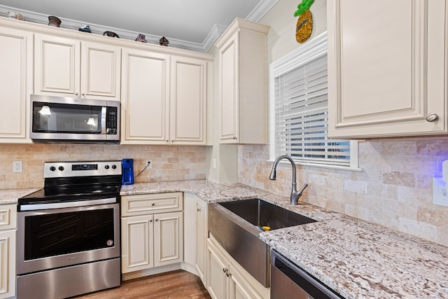 kitchen with cream cabinetry, stainless steel appliances, light stone countertops, and crown molding