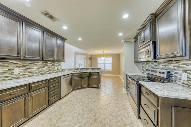 kitchen with appliances with stainless steel finishes, backsplash, hanging light fixtures, dark brown cabinets, and ornamental molding