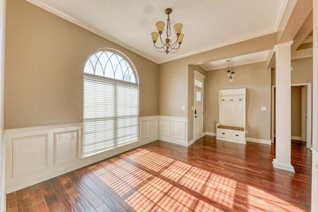 spare room featuring hardwood / wood-style flooring, crown molding, a chandelier, and ornate columns