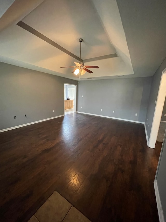 spare room featuring a ceiling fan, a raised ceiling, baseboards, and dark wood-style flooring