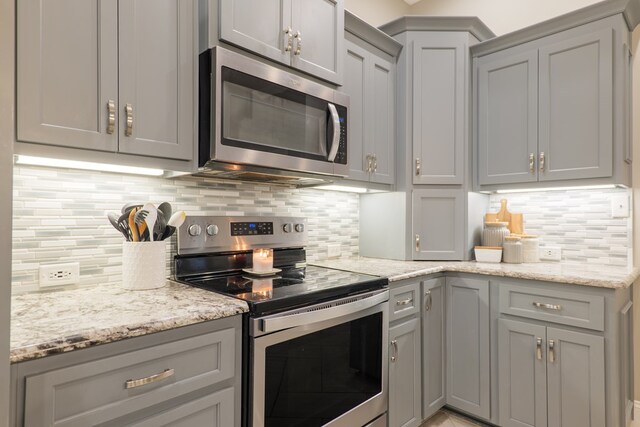 kitchen featuring decorative backsplash, appliances with stainless steel finishes, light stone countertops, and gray cabinetry