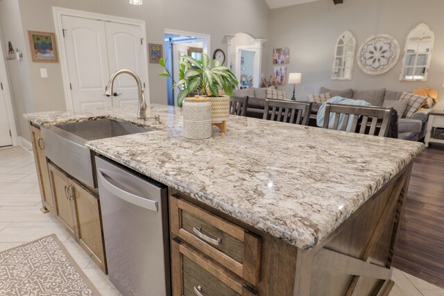 kitchen featuring light stone counters, sink, light tile patterned floors, a center island with sink, and dishwasher