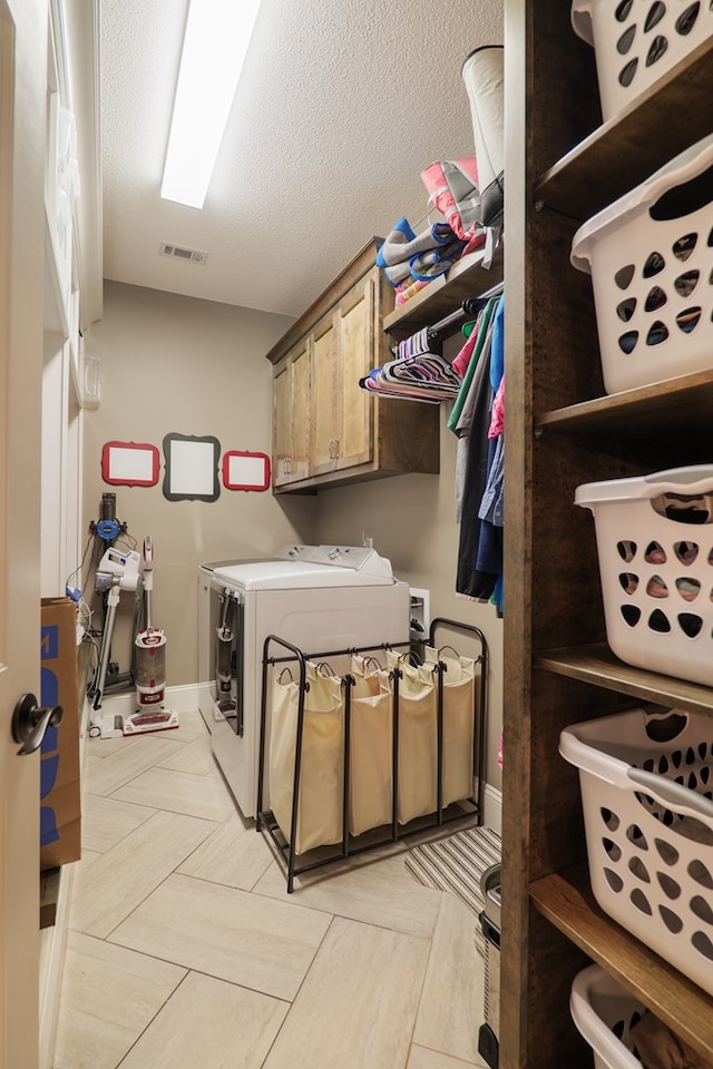 clothes washing area featuring cabinets, light tile patterned floors, washer and dryer, and a textured ceiling