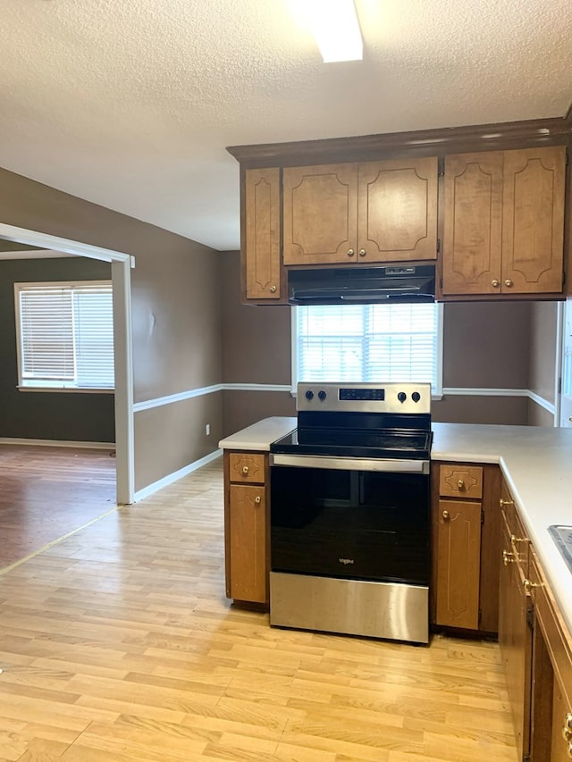 kitchen featuring stainless steel electric range oven, range hood, light hardwood / wood-style flooring, and a textured ceiling