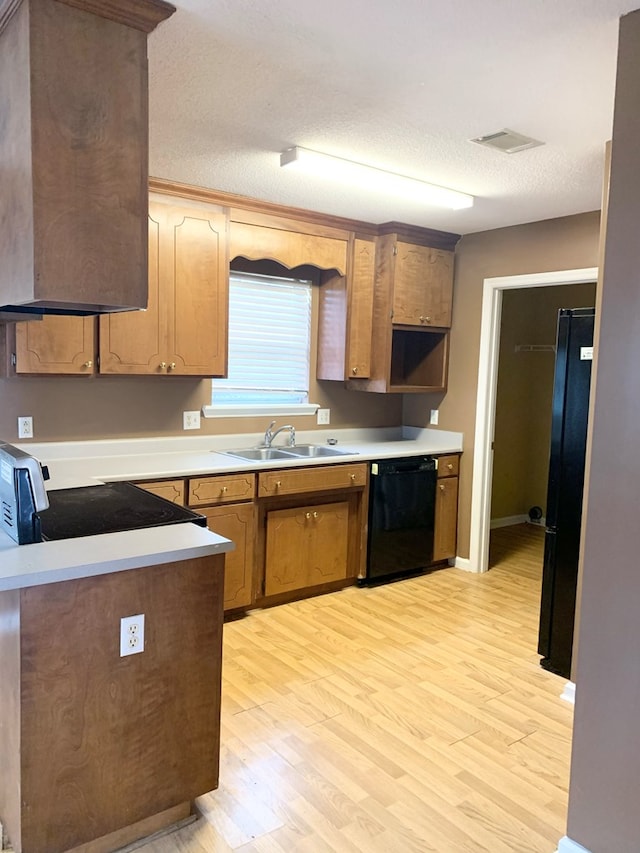 kitchen featuring sink, light hardwood / wood-style flooring, a textured ceiling, and black appliances