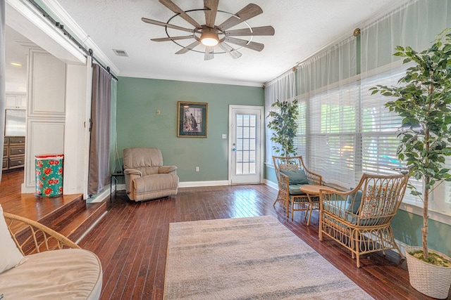 living area featuring ceiling fan, visible vents, hardwood / wood-style flooring, a barn door, and ornamental molding