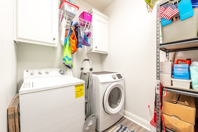 clothes washing area featuring washing machine and clothes dryer, cabinets, and light wood-type flooring