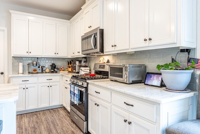 kitchen featuring white cabinets, light wood-type flooring, stainless steel appliances, and tasteful backsplash