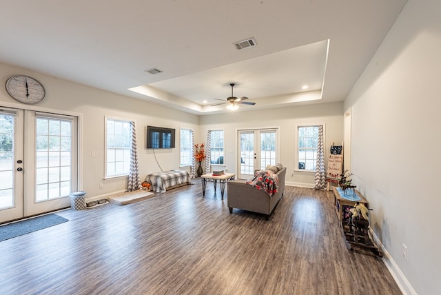 living room with a tray ceiling, dark hardwood / wood-style flooring, ceiling fan, and french doors