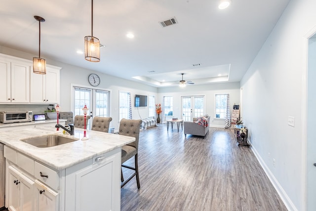 kitchen with a tray ceiling, white cabinetry, french doors, and an island with sink