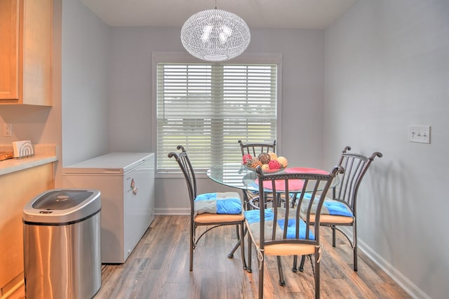 dining space with baseboards, a healthy amount of sunlight, light wood-style flooring, and an inviting chandelier