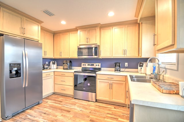 kitchen with light brown cabinets, a sink, appliances with stainless steel finishes, light wood finished floors, and light countertops