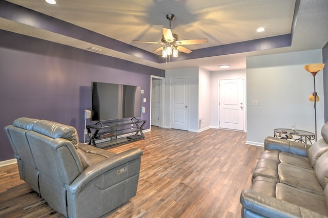 living area featuring ceiling fan, a raised ceiling, baseboards, and wood finished floors