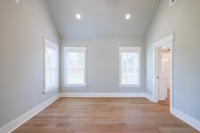 spare room with a healthy amount of sunlight, high vaulted ceiling, and light hardwood / wood-style flooring