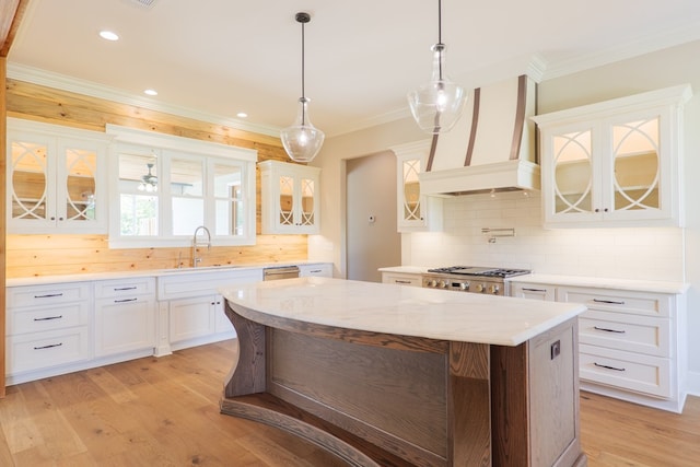 kitchen featuring premium range hood, white cabinetry, sink, hanging light fixtures, and a center island