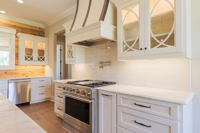 kitchen with ornamental molding, appliances with stainless steel finishes, custom exhaust hood, and white cabinets