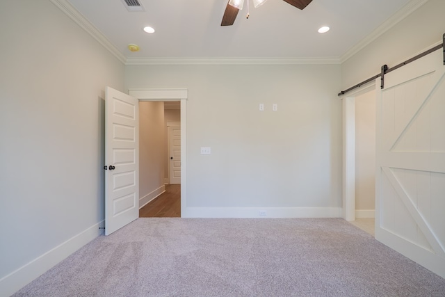 unfurnished bedroom with crown molding, ceiling fan, a barn door, and carpet