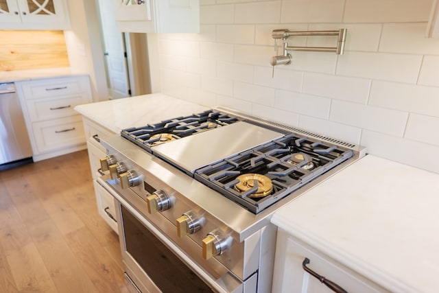 kitchen with dishwasher, backsplash, white cabinets, high end range, and light hardwood / wood-style floors