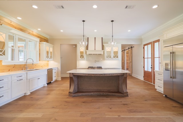 kitchen with appliances with stainless steel finishes, white cabinetry, hanging light fixtures, custom exhaust hood, and a barn door