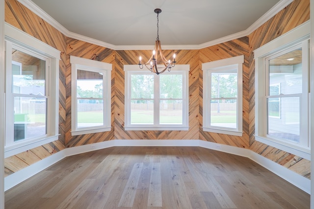 unfurnished dining area with an inviting chandelier, ornamental molding, wood-type flooring, and a wealth of natural light