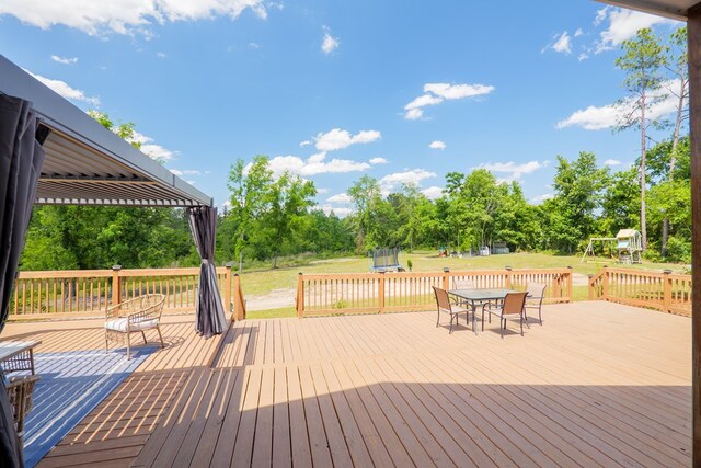 4310 Old Quitman Hwy, Valdosta, GA 31601 - wooden deck with a trampoline, a playground, a yard, outdoor dining space, and view of wooded area