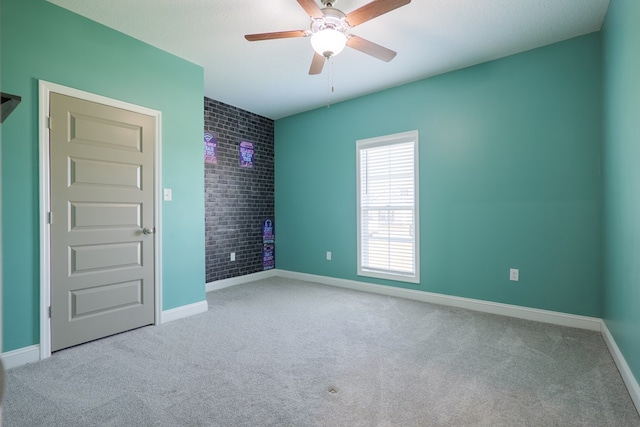 empty room featuring carpet, baseboards, brick wall, and ceiling fan